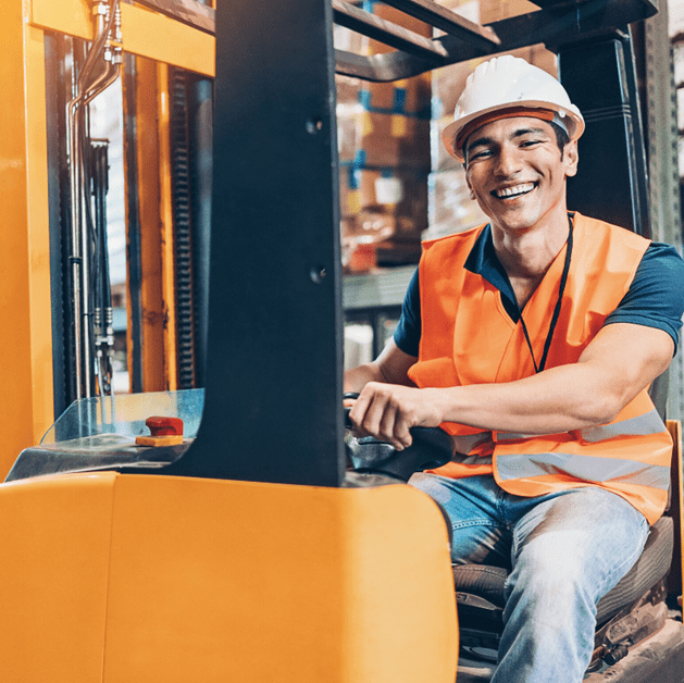 Man wearing a construction hard hat and driving a forklift in a warehouse